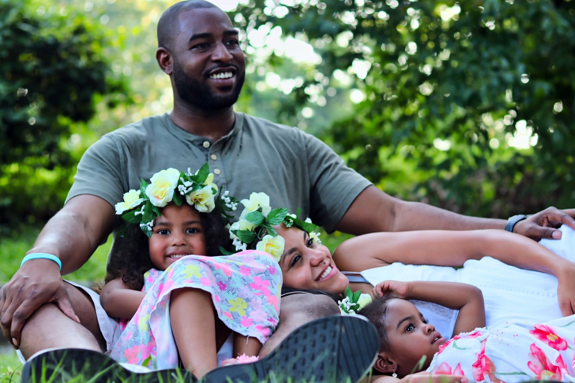 Father sitting in the grass with his 2 daughters and wife sitting or resting on his lap