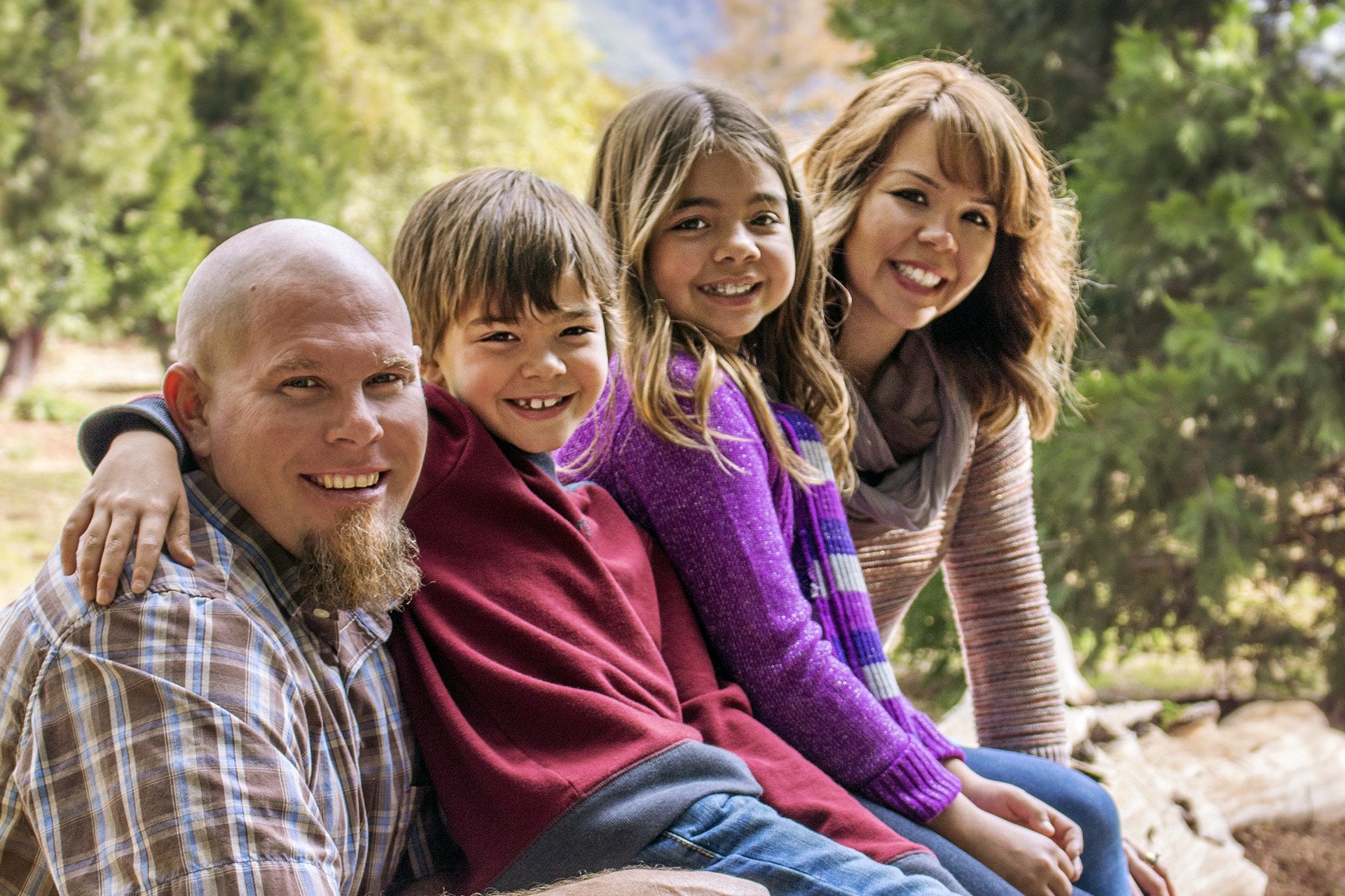 Family sitting on a log in the woods smiling