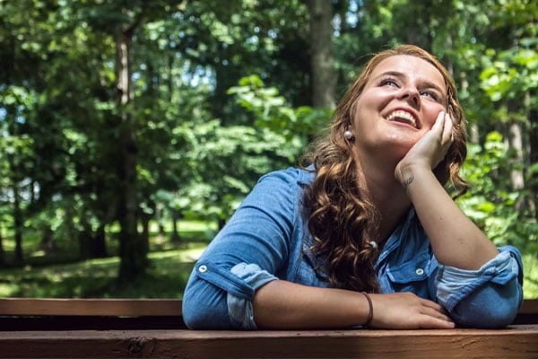 happy female sitting at picnic table smiling at the sky in the woods