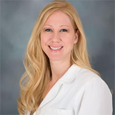 Jessica young, blonde female wearing a white professional jacket sitting in front of a gray background
