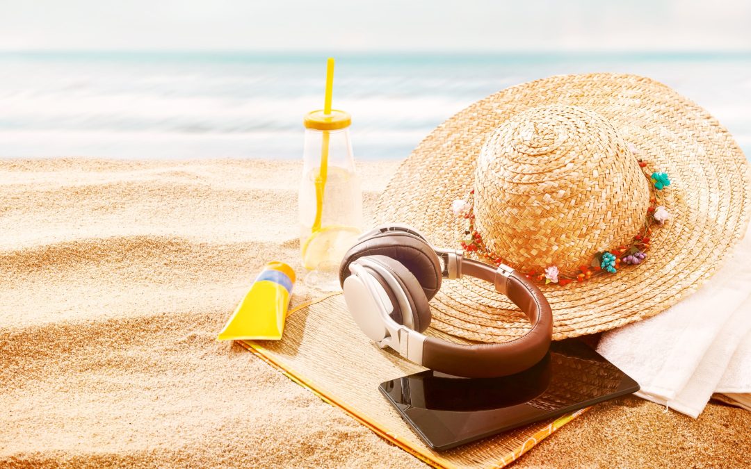 A noise canncelling headphone set on a beach with a hat cellphone and sunscreen